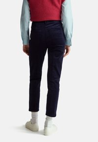 Navy corduroy pants with a slim fit, featuring back pockets and a slightly cropped length, paired with white sneakers and ribbed socks.