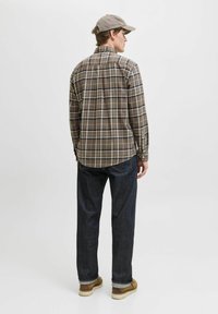 Brunternet flannel skjorte med knapmanchetter, sat sammen med mørke jeans og beige sko. Skjorten har en buet kant og rygplissé.
