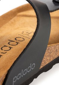 Sandale avec sangle synthétique noire, semelle en liège, doublure texturée marron et semelle en caoutchouc. Présente le logo "palado" sur le côté.
