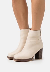 Beige semišové kotníkové boty s kulatou špičkou, s manžetou a se zúženým dřevěným podpatkem. Boční zip pro snadné obouvání.
