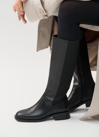 Botas pretas até ao joelho feitas de couro liso, com painéis laterais el�ásticos e um salto baixo, apresentando um fecho lateral para facilitar o calçar.