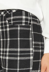 Calças às riscas em preto e branco com um tecido texturizado, apresentando um bolso lateral e um design estruturado.