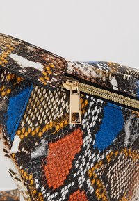 Sac à main avec motif en peau de serpent multicolore, fermeture éclair dorée et texture d'écailles noires, orange, bleues, blanches et jaunes.