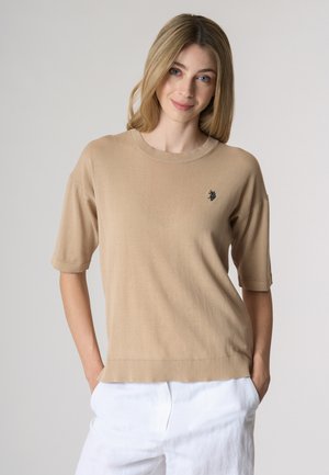 Maglione a maniche corte beige in maglia con scollo rotondo e orlo a coste. Presenta un piccolo emblema nero sul lato sinistro del petto.