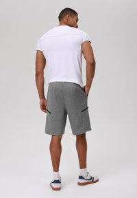 Šedé sportovní kraťasy se bočními kapsami, doplněné o bílý přiléhavý tričko. Model je otočen zády, což ukazuje jednoduchý design a ležérní vzhled.