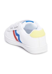 Biała sneakersy z gładką syntetyczną cholewką. Posiadają czerwone, niebieskie i żółte akcenty, okrągły czubek oraz teksturowaną gumową podeszwę.