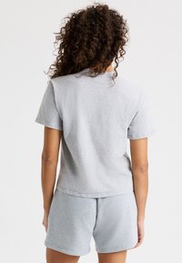 Camiseta de algodón gris con mangas cortas, corte relajado y escote redondeado. Se lleva con unos pantalones cortos de algodón gris a juego.