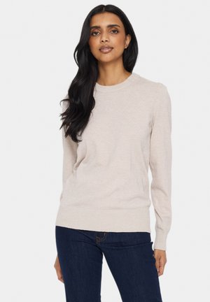 Lichtbeige gebreide trui met een ronde halslijn, lange mouwen en een ribgebreide zoom. Zachte textuur; gepresenteerd met donkerblauwe jeans.