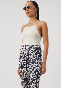 Baltos satino halter top'as, derinamas su tamsiai mėlynomis kelnėmis, turinčiomis baltą keistos formos raštą. Priedai - šviesūs saulės akiniai.