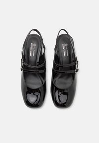Scarpe slingback in vernice nera con due fascette frontali, punta rotonda e interno imbottito. Materiale vegano, finitura lucida e slanciata.