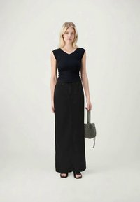 Black sleeveless top with a V-neck, paired with a long black skirt, black sandals, and a small black and white patterned bag.