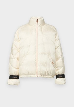 Giacca puffer color crema con colletto alto e zip in oro rosa. Presenta polsini elastici con accenti neri del marchio e una vestibilità cropped.