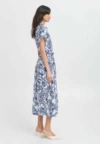Rochie cu model paisley alb și albastru, cu mâneci scurte, talie cu curea și lungime midi, asortată cu pantofi cu toc joș ușori.