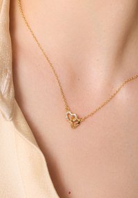 Złoty naszyjnik z łańcuszka z dwoma wkleszonymi charmsami serca; jeden z przezroczystymi cyrkoniami, drugi gładki. Dyskretne połyski, delikatny design.