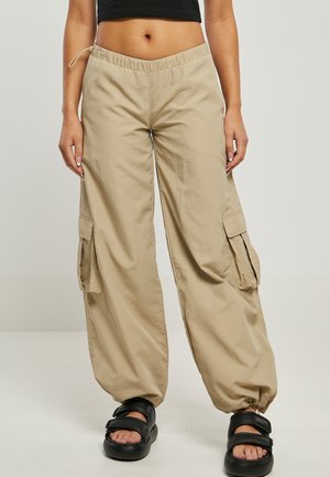 Pantalones cargo beige con cinturilla elástica, dos bolsillos laterales y puños fruncidos, fabricados con material ligero, combinados con sandalias negras.