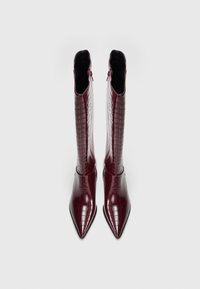 Bordo krāsas zābaki ar smailu purngalu, spīdīgu krokodila ādas rakstu, kas sniedzas līdz teļa vidum un aprīkoti ar sānu rāvējslēdzējiem aizvēršanai.