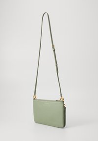 Borsa a tracolla in pelle verde chiaro con una texture liscia, dettagli in metallo dorato e una tracolla regolabile; presenta una chiusura con zip e un marchio discreto.