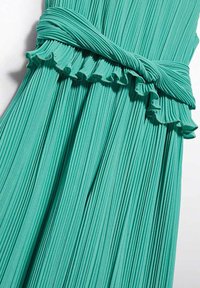 Abito verde plissettato con scollatura arricciata e vita legata. Il tessuto presenta linee verticali, creando un aspetto strutturato.