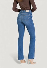 Jean en denim bleu taille haute avec une silhouette ajustée. Comprend deux poches arrière et une étiquette à la ceinture. Associé à des talons hauts couleur nude.