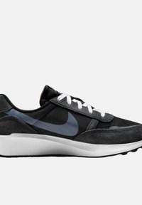 Zapatilla negra y gris con materiales de textil y ante, cordones blancos, acentos reflectantes y suela blanca. Presenta el logo de Nike en gris oscuro.