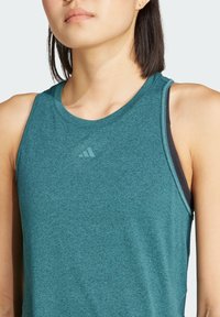 Débardeur de sport teal en tissu texturé, avec un col rond et un sous-vêtement noir superposé, et des détails de logo subtils.