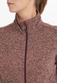 Tight sittande jacka med dragkedja i en texturerad, melerad rosa tyg med hög krage och mörkröda dragkedjedetaljer. Har flatlock-sömmar för ökad komfort.