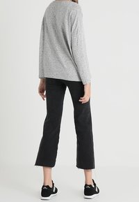 Graues Langarmoberteil mit lockerer Passform, kombiniert mit schwarzen, knöchellangen Jeans mit fransigem Saum und schwarzen Sportschuhen.