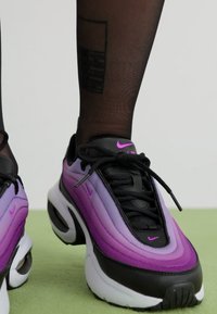  svarte og lilla Nike joggesko med gradient tekstur, rund tå, snøring, og polstret såle. Har en svart nettingøvre og rosa detaljer.