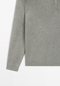 Hellgrauer Strickpullover mit langen Ärmeln, gerippten Bündchen und Saum sowie einem teilweisen silbernen Reißverschluss am Ausschnitt vor weißem Hintergrund.