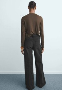 Top marrón de manga larga combinado con jeans negros de tiro alto y pierna ancha. El top tiene una textura suave y los jeans cuentan con bolsillos traseros.