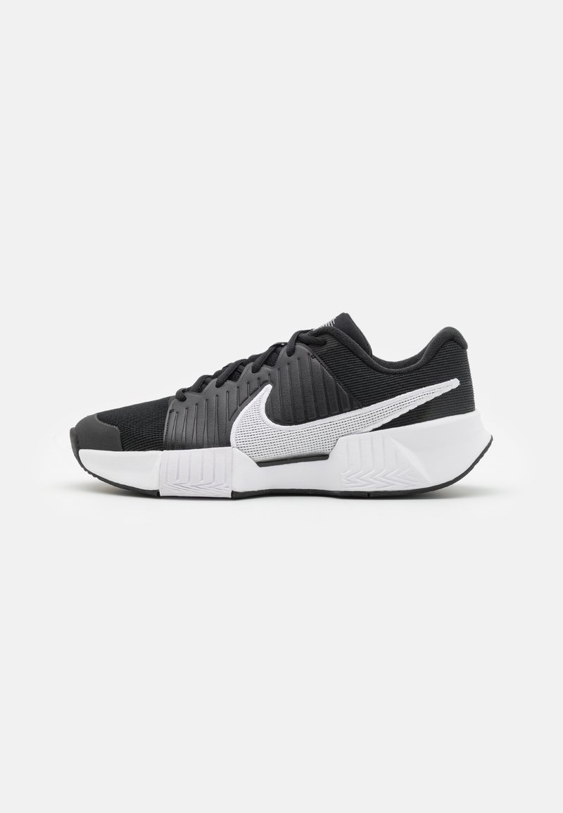 Sapatos atléticos pretos com um cabedal texturizado, logótipo swoosh branco, calcanhar acolchoado e uma sola branca em contraste com um padrão em zigzag.