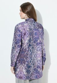 Langarmshirt in paarse, blauwe en witte abstracte patroon. Heeft een hoge kraag, knoopsluiting bij de mouwen en een rechte snit.