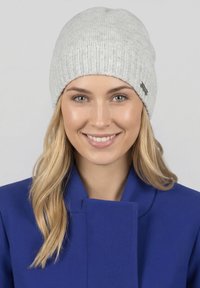 Graue gerippte Mütze aus Strickmaterial mit nahtlosem Oberteil und kleinem Logotag. Der Träger hat blonde Haare und trägt eine blaue Jacke.