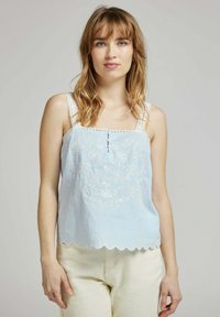 Débardeur en coton bleu clair avec broderies florales blanches, ourlet festonné et bretelles en dentelle décoratives. Comprend un détail de bouton à l'avant.