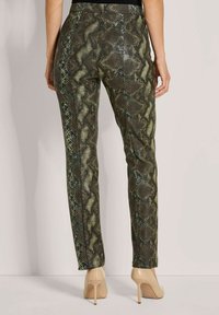 Slangenhuidprint broek in groen en bruin, met een aansluitend ontwerp. Het materiaal heeft een glanzende textuur, gecombineerd met naaktschoen met hoge hakken.