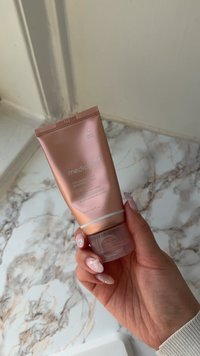Main tenant un tube en or rose de la masque Collagen Impact Wrapping Mask de medicube sur un fond de plan de travail en marbre.