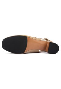 Chaussure à talons beiges avec une semelle en caoutchouc noir, au design épuré et dotée d'une sangle réglable avec un détail de boucle en or.