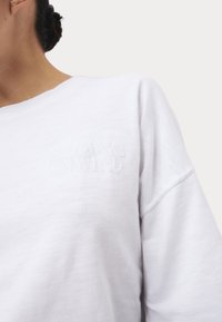 Weißer Sweatshirt aus weichem Stoff, mit lockerer Passform, gesenkten Schultern und geprägtem Text "RELAX & UNWIND" auf der Vorderseite.