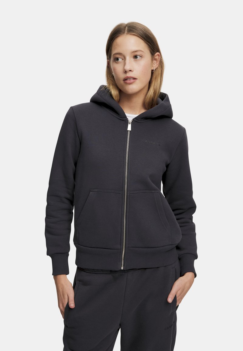 Mørk grå zip-up hettegenser i myk stoff, med en frontlomme og ribbet mansjetter. Inkluderer hette med snor og subtil merking på brystet.