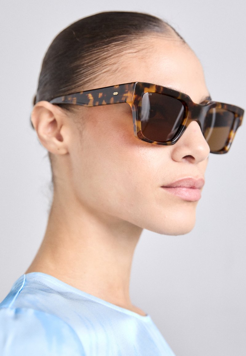 Tortoiseshell sunglasses with a chunky, rectangular frame. Dark lenses and gold-tone accents on the temples. Smooth, glossy finish.