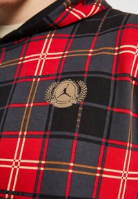 Felpa con cappuccio a quadri rossi, neri e grigi in tessuto morbido, caratterizzata da un badge logo con una silhouette e un design di alloro sul petto.