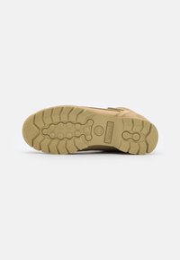 Bota de color beige claro con una suela de goma texturizada que presenta profundas marcas y un patrón moldeado. Incluye un tobillo reforzado y ojetes de metal.