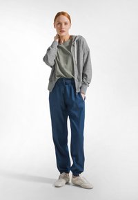 Grå zip-up hoodie, grön t-shirt under, lösa blå joggers och beige sneakers. Mjukt tyg, avslappnad passform och elastisk midjeresår.