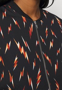 Černá bomber bunda s živým vzorem blesků v červené, oranžové a bílé. Obsahuje přední zip a žebrovaný límec.