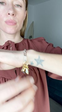Silver charm bracelet featuring gold accents and multiple decorative charms, displayed on a wrist with a star tattoo.
