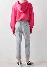 Sweatshirt à capuche rose avec des manches larges, associé à un pantalon gris clair fuselé avec des poches latérales et des poignets en côtes grises. Baskets noires et blanches.