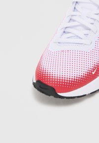 Fehér és piros sportcipő, texturált pöttyös mintával, kontrasztos fekete gumitalppal és fehér fűzőkkel. Kerek orrú dizájnnal rendelkezik.
