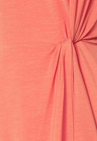 Tissu corail avec un nœud froncé créant de doux plis et un drapé texturé sur un matériau lisse et extensible.