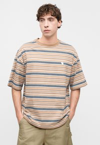 Καφέ ριγέ κοντομάνικη μπλούζα, με οριζόντιες μπλε και άσπρες ρίγες, στρογγυλή λαιμόκοψη και μικρό λογότυπο στο στήθος.