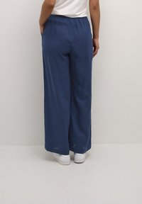 Navy blue wide-leg pants with an elastic waistband, made of lightweight fabric. Styled with white sneakers, viewed from the back.
